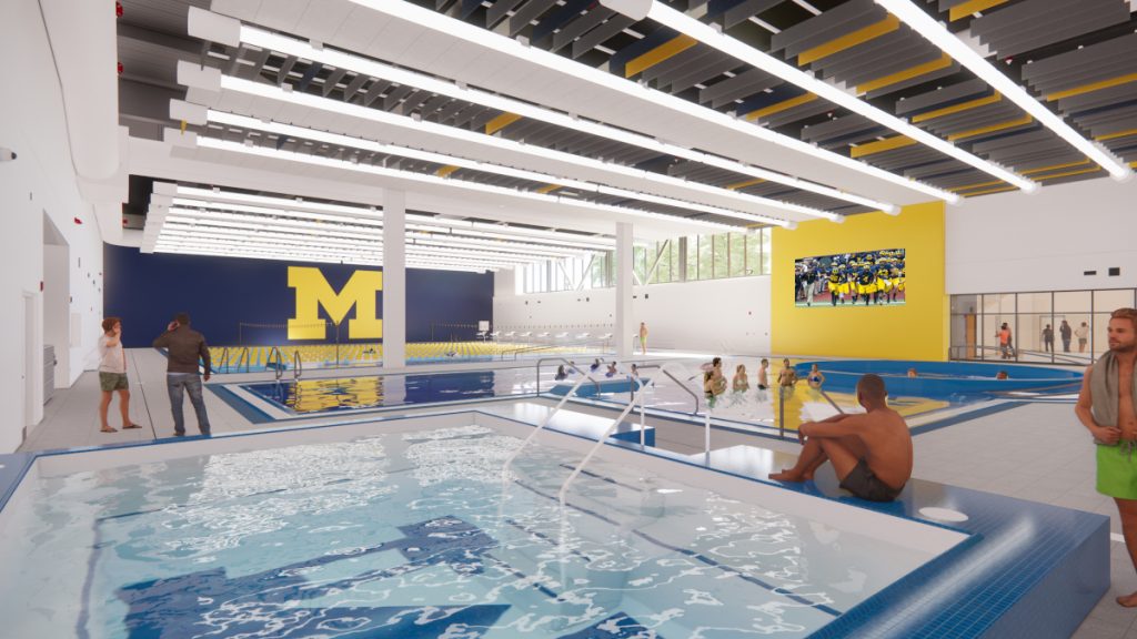Indoor swimming facility featuring multiple pools, people relaxing and socializing, and large maize-and-blue University of Michigan logos.