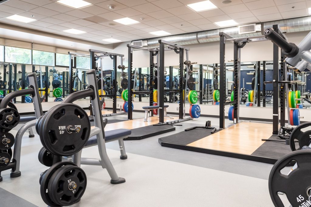 Weightlifting area with racks, benches, and colorful plates.