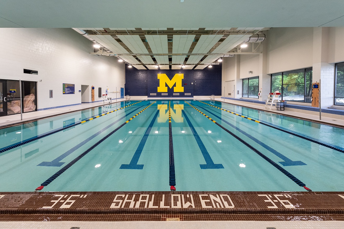 Indoor pool with lane markers, large maize “M,” and windows.