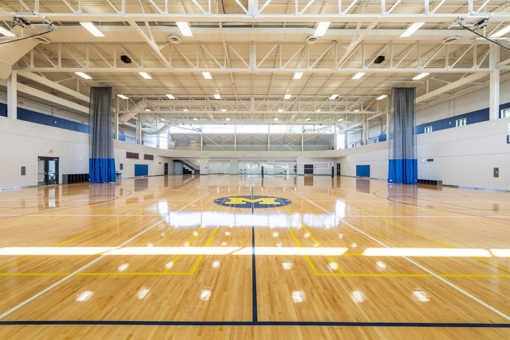 Spacious court with polished floors, blue-and-maize markings, and high ceiling lighting.