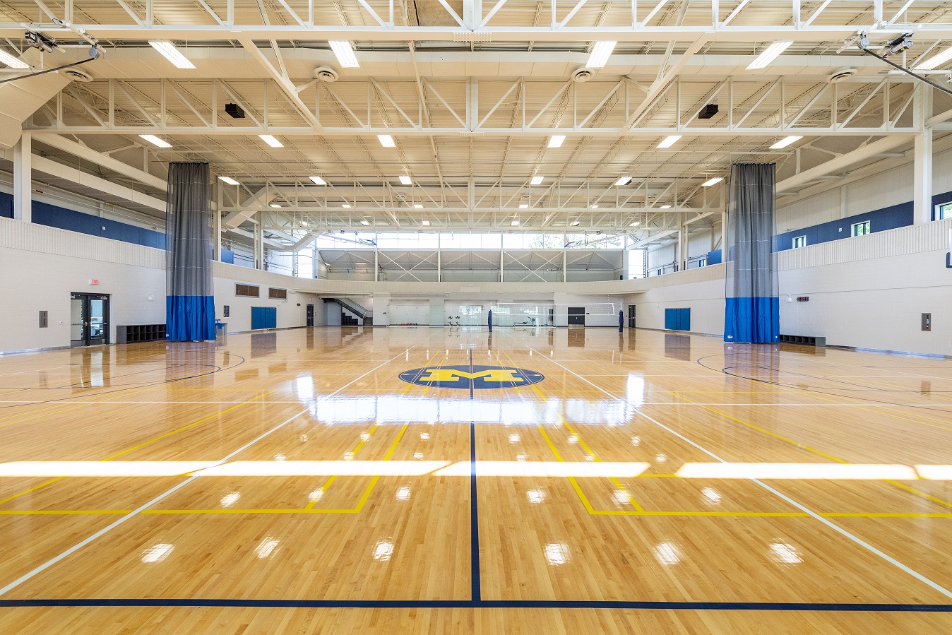 Spacious court with polished floors, blue-and-maize markings, and high ceiling lighting.