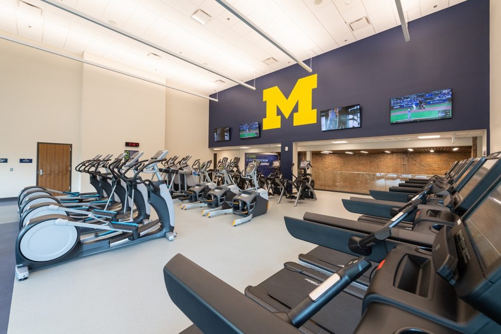 Cardio room with treadmills, ellipticals, and maize “M” logo.