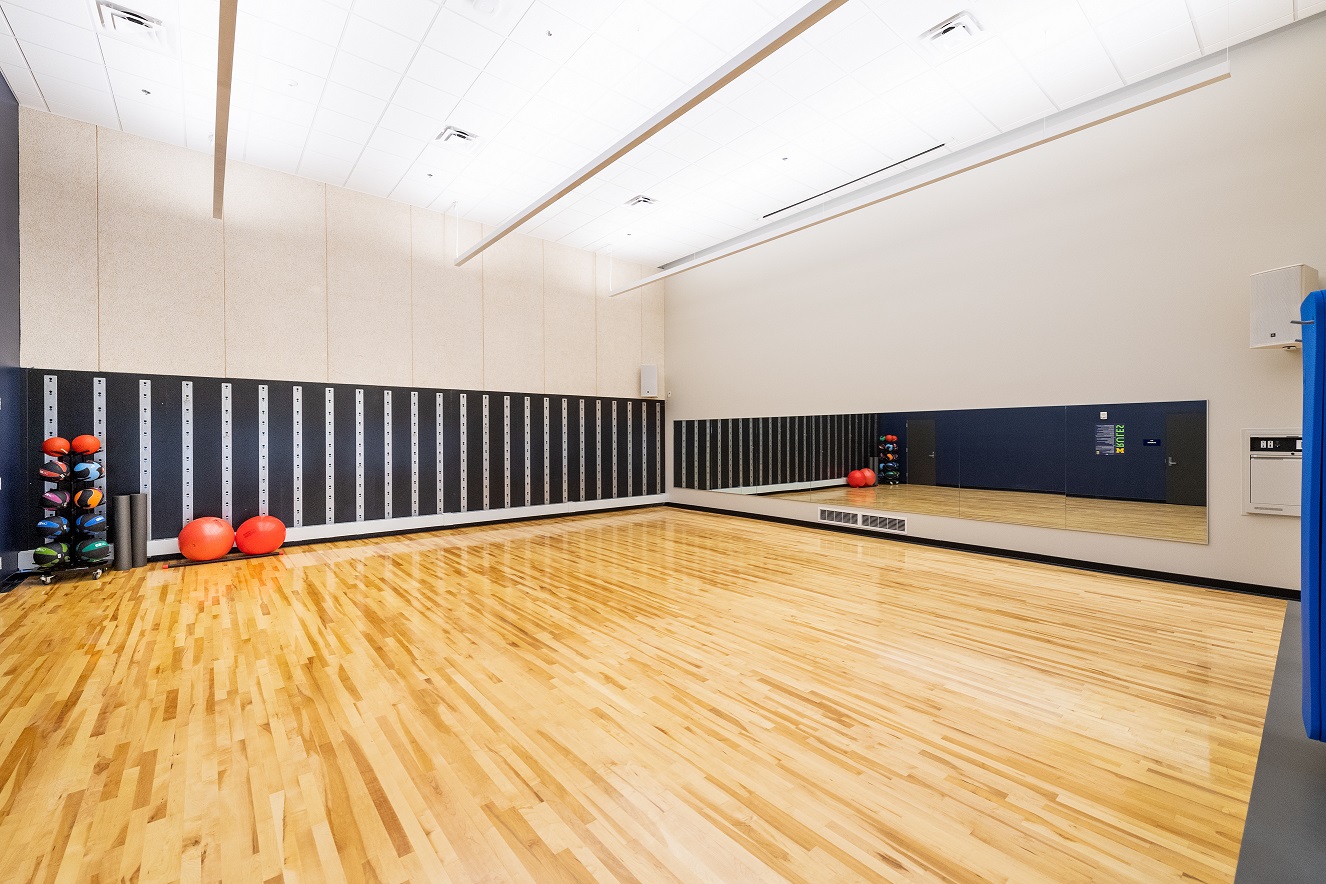 Clean group fitness space with mirrored walls, hardwood flooring, lockers, and two red exercise balls.