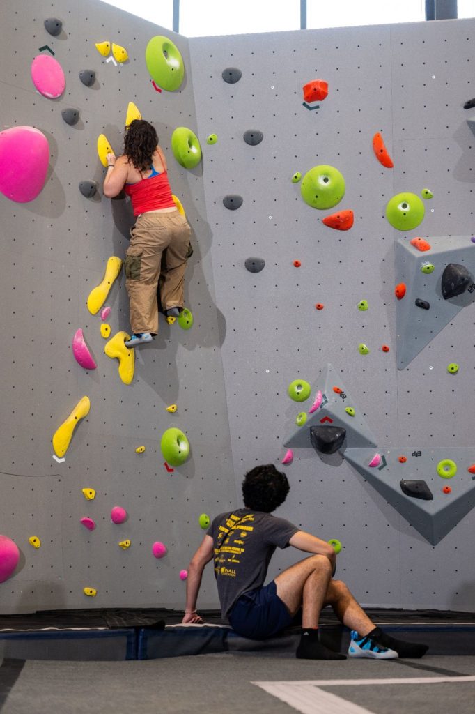 Two people climbing an indoor rock wall with colorful climbing holds.
