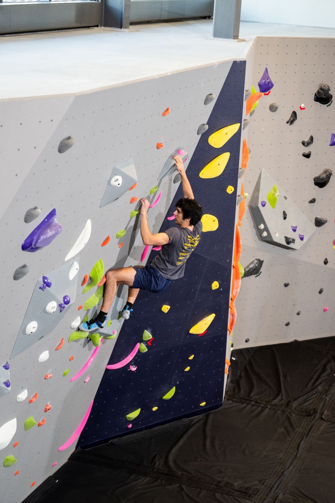 A person climbing an indoor rock wall with colorful climbing holds