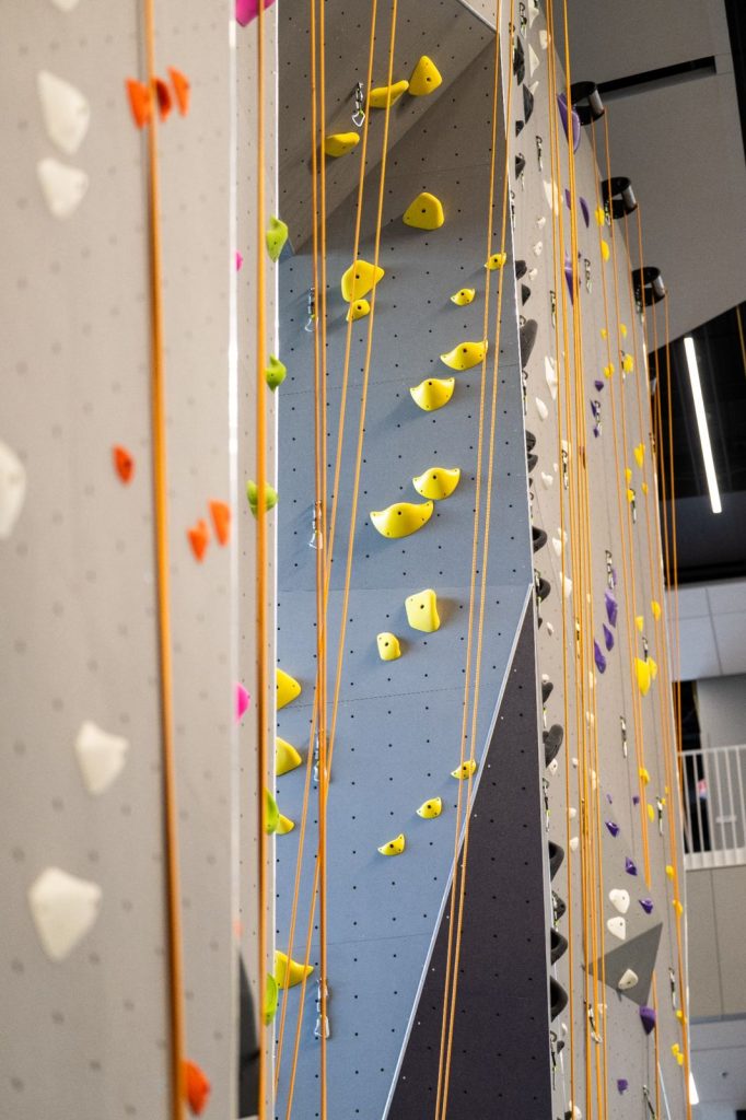 Indoor rock climbing walls with yellow and orange climbing holds and hanging ropes