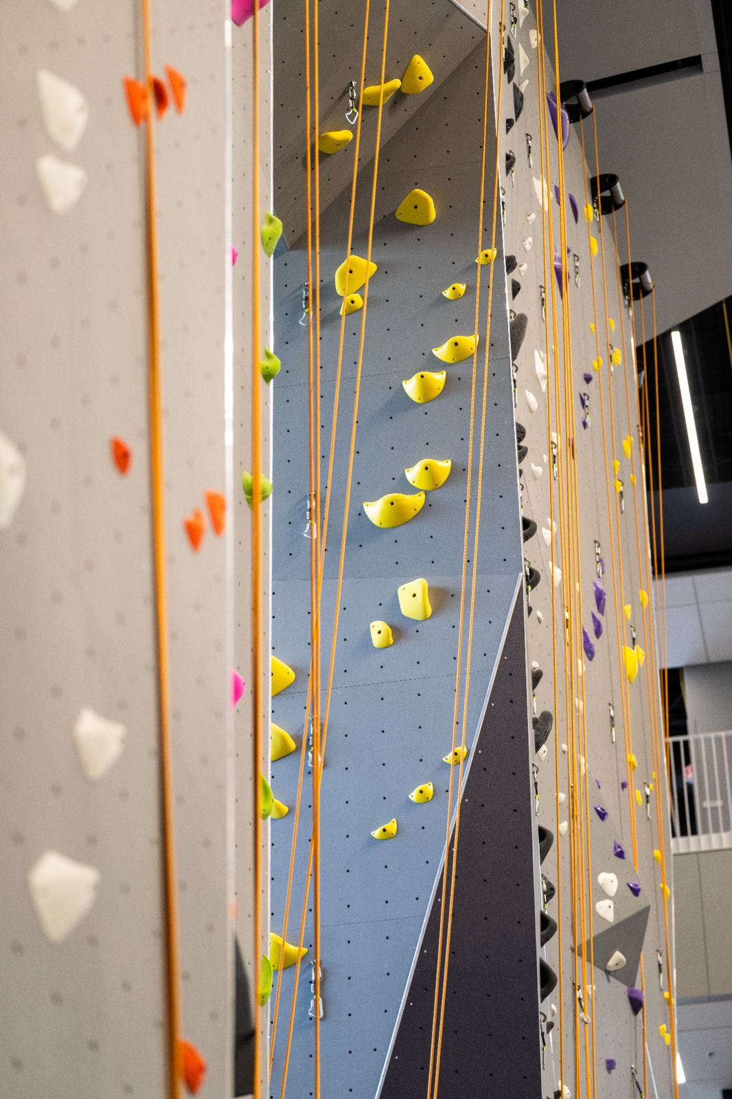 Indoor rock climbing walls with yellow and orange climbing holds and hanging ropes