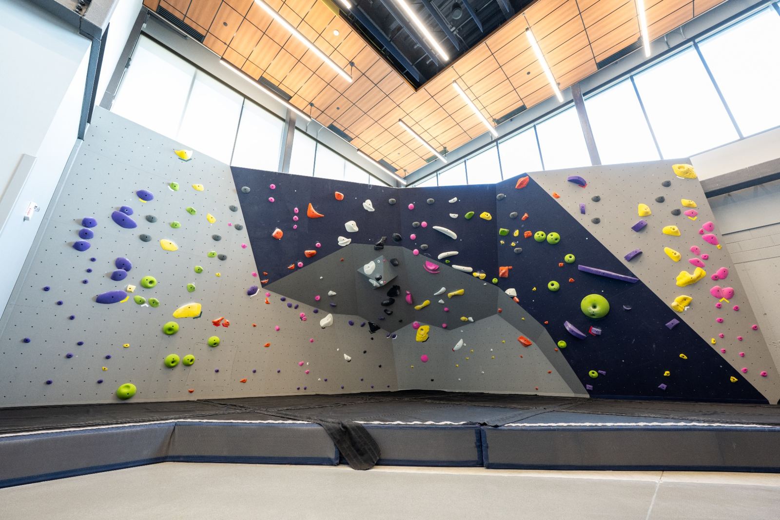 Indoor bouldering wall with colorful climbing holds, a geometric design, and padded flooring