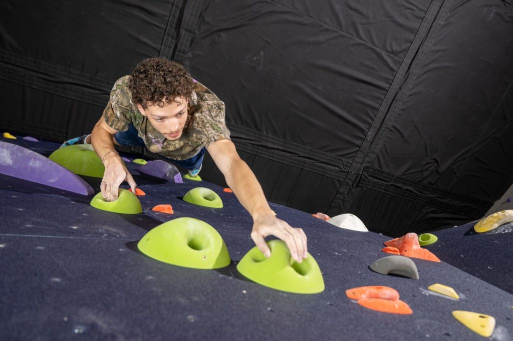 A person climbing an indoor bouldering wall, gripping bright green climbing holds