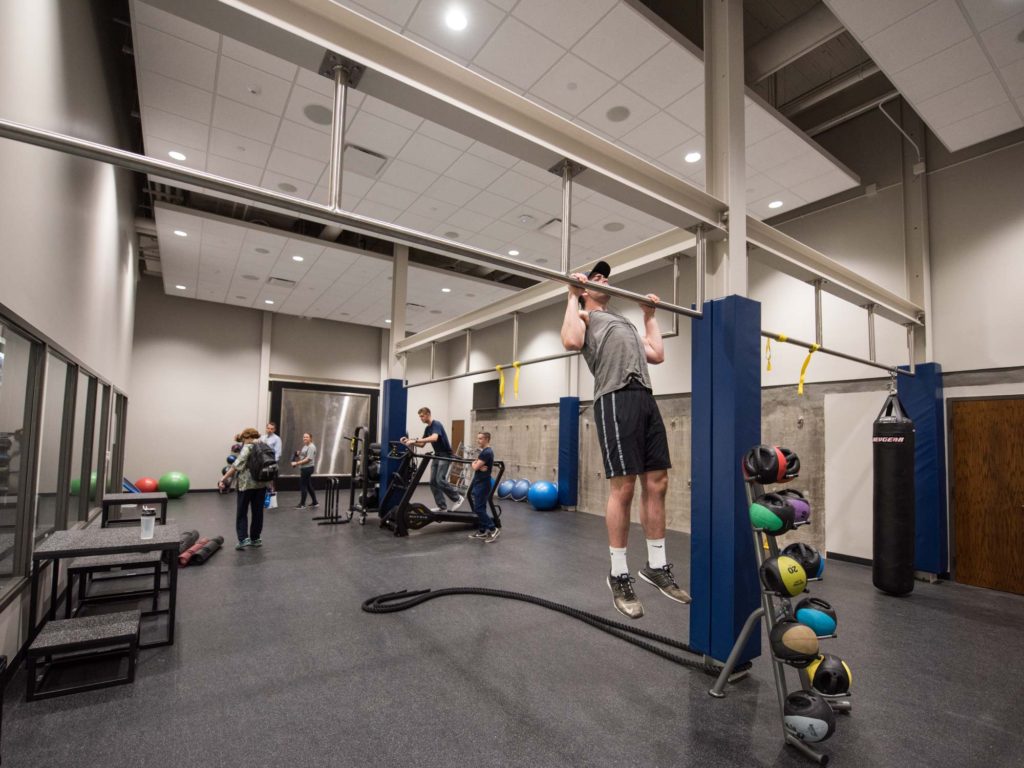 Room with fitness equipment, pull-up bars, and people exercising.