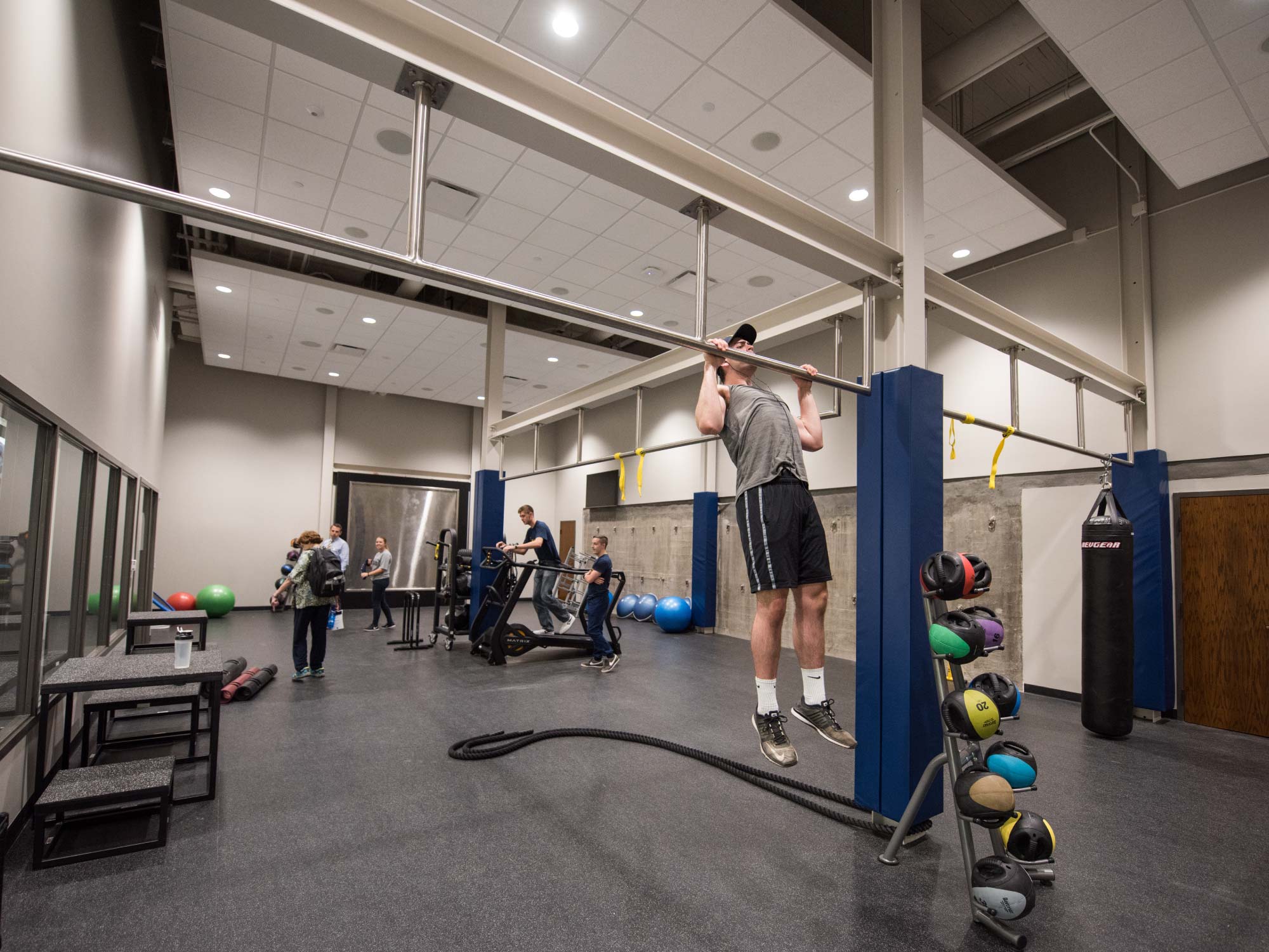 Room with fitness equipment, pull-up bars, and people exercising.