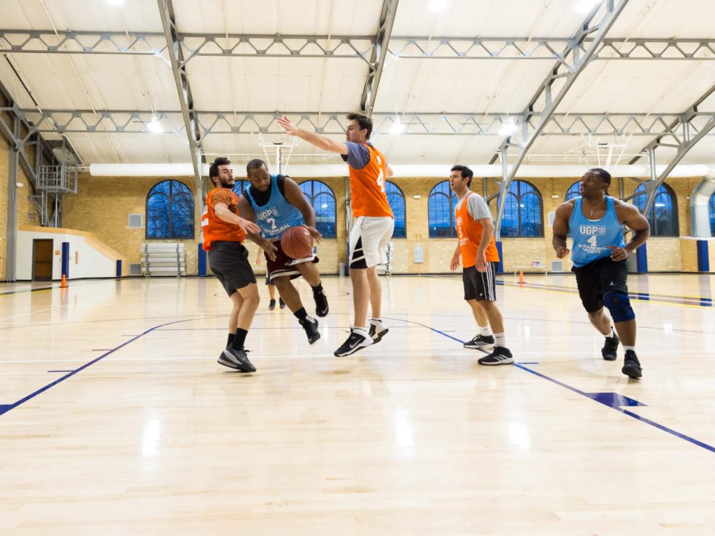 Group of players competing in a basketball game in a gymnasium with arched windows and high ceilings;